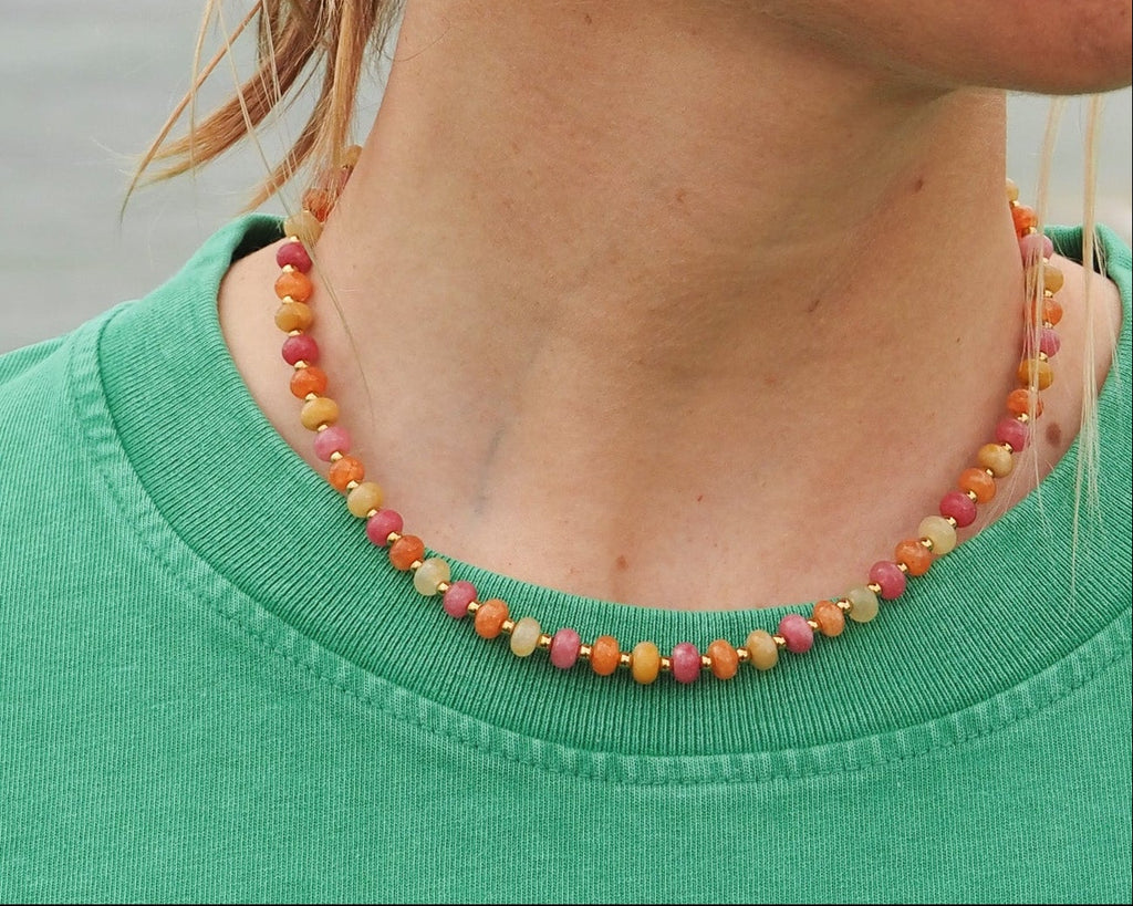 Woman wearing a colorful beaded necklace and gold hoop earrings with a blurred natural background